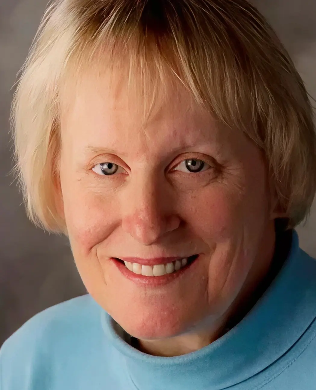 Portrait of a smiling elderly woman with light hair and blue sweater.