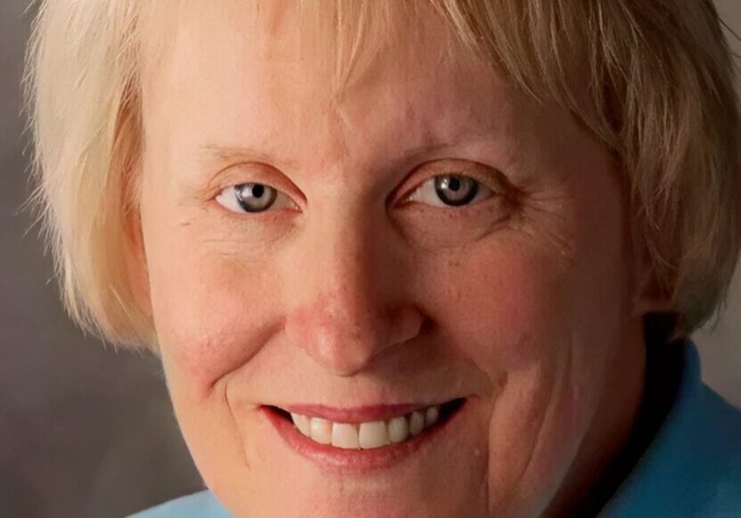 Portrait of a smiling elderly woman with light hair and blue sweater.
